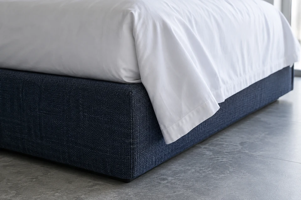 Low view of white bed linen touching the corner of an indigo upholstered hotel bed base