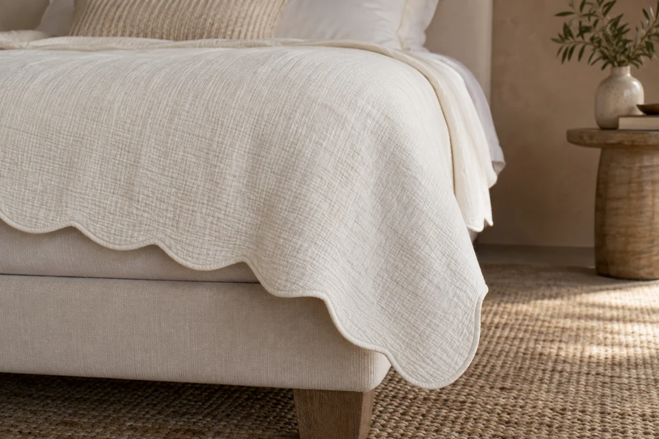 An ivory bedspread with a neatly finished scalloped edge hangs over an upholstered bed corner